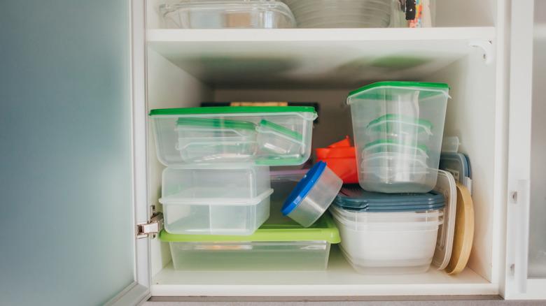 plastic tupperware food storage containers precariously perched in white kitchen cabinets