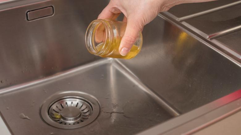 Someone pouring oil down a kitchen sink