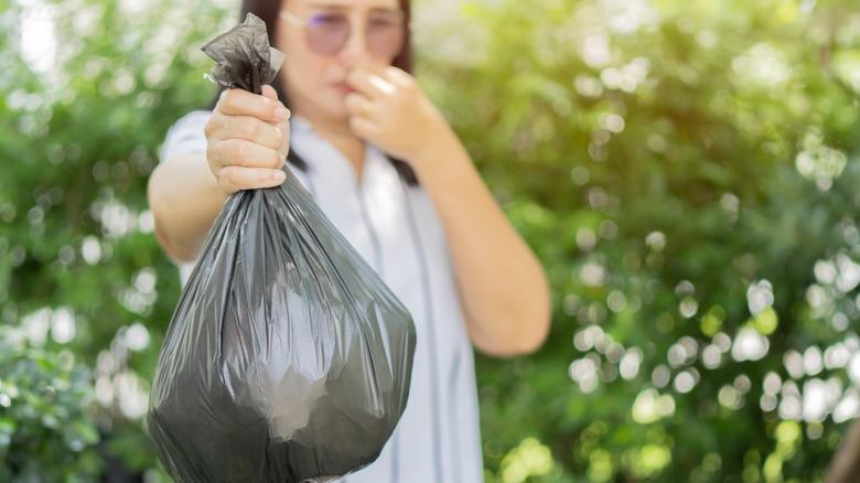 Woman with a trash bag and holding her nose