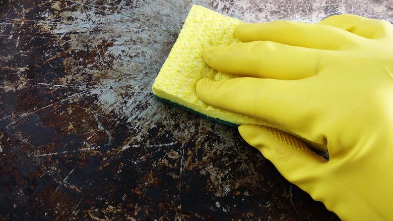 A yellow-gloved hand scrubbing discolored pan with sponge