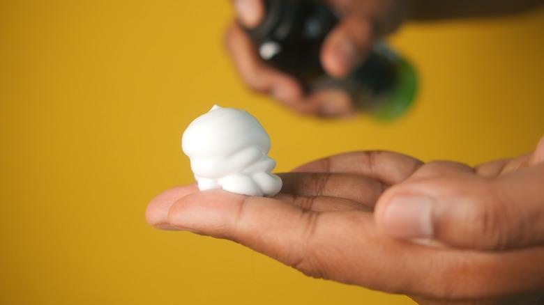 Someone with a pile of shaving cream in their hand against a yellow background