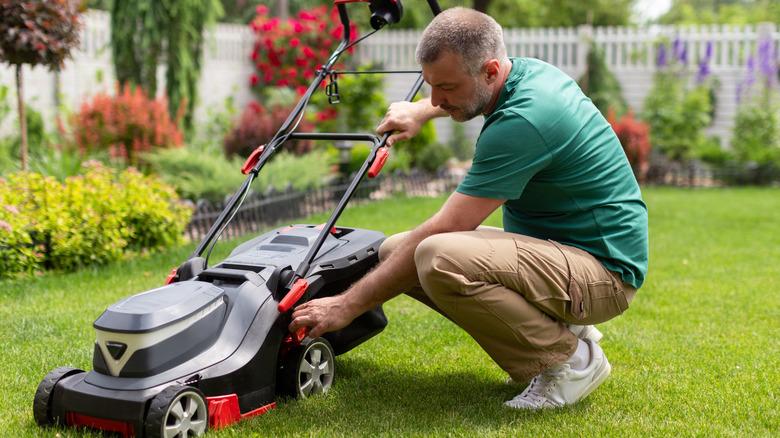 Man inspecting lawn mower in yard