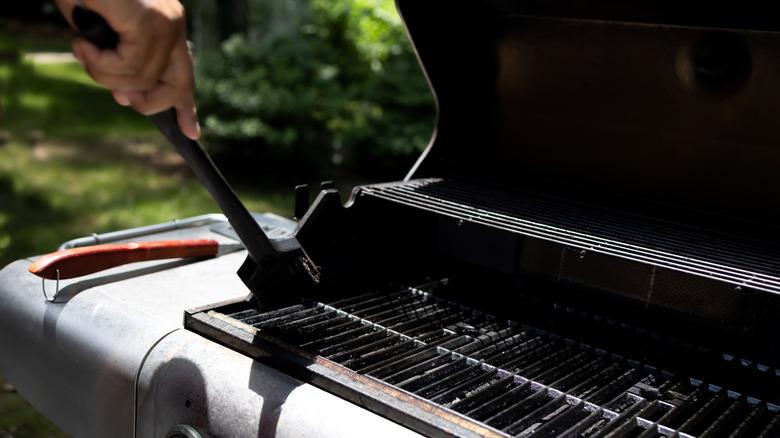 A hand cleaning a grill grate with brush