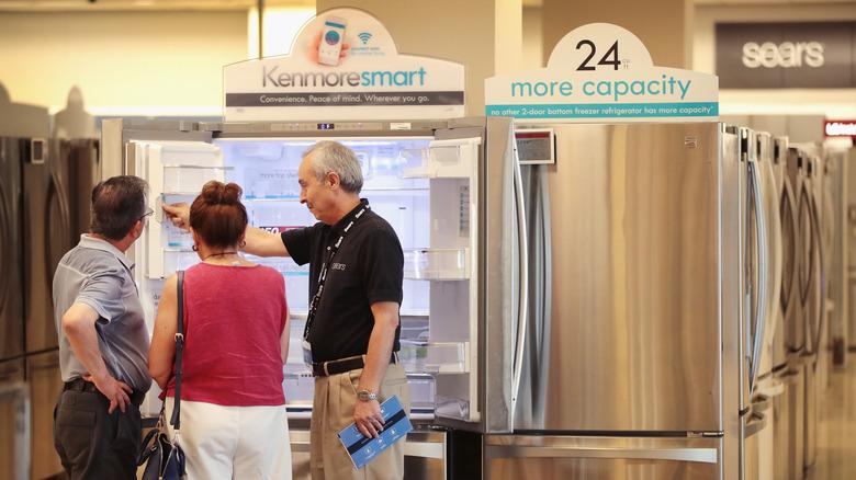 a couple shopping at a Sears store for a stainless steel Kenmore french door smart refrigerator and being helped by an older male salesman