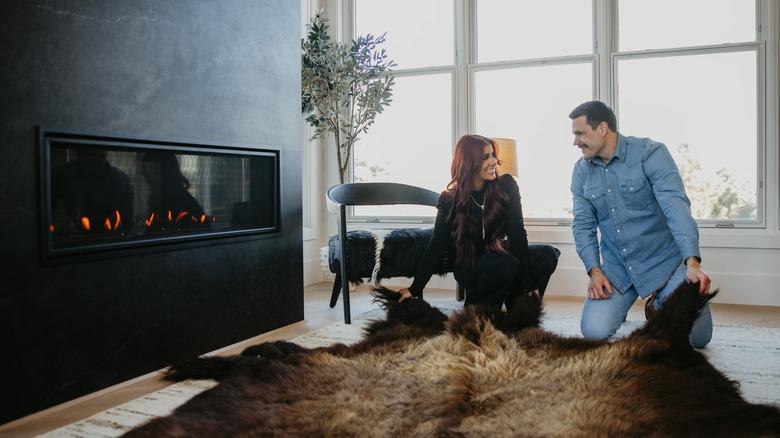 Chelsea and Cole DeBoer placing a cowhide rug in front of a black fireplace
