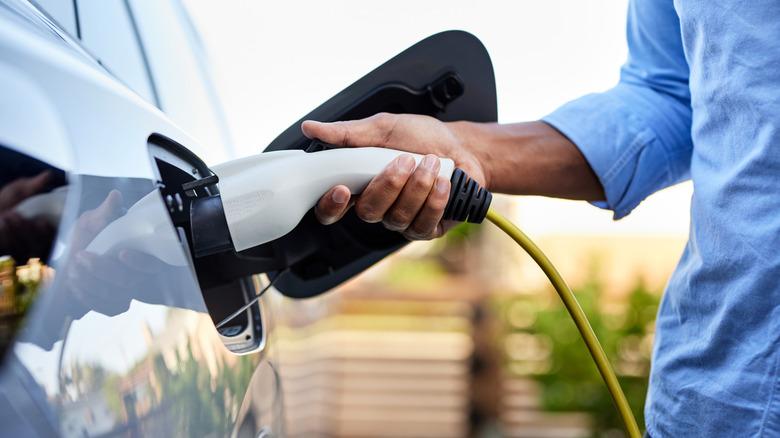 An anonymous hand of someone wearing a blue shirt inserts an EV charger into their car.