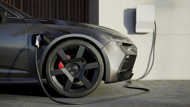 A black electric vehicle is plugged into a wall-mounted EV charger at someone's home.