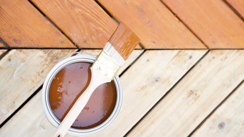 close up of wooden patio with bucket of stain and dirty paint brush