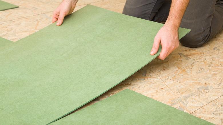 hands laying green flooring over plywood subflooring