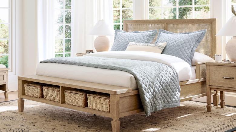 bedroom with wood nightstands and bed that features a tall cane headboard, integrated armrests for stability, and built-in storage bench at the end