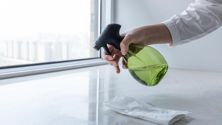 hand spraying windowsill with bottle