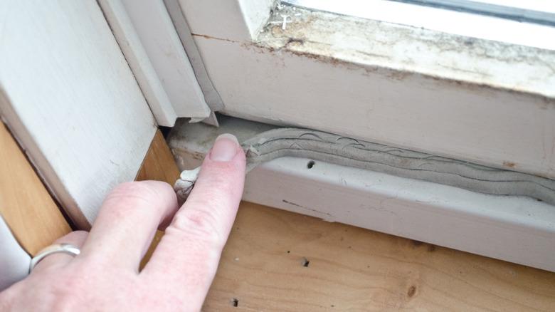 person's hand checking window caulking