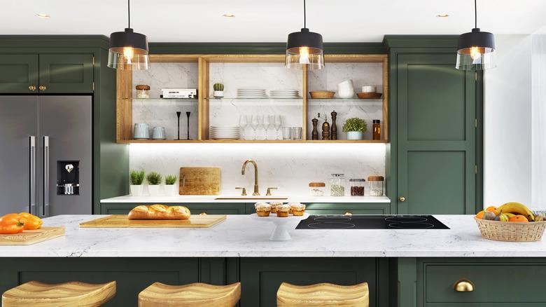 modern kitchen with dark green cabinetry, marble countertops, and natural wood open shelving above a gold faucet that is minimalistically styled with white and wood kithchenware