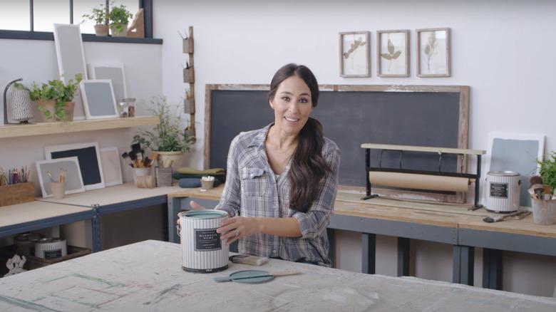 Joanna Gaines holding a paint can on a work table