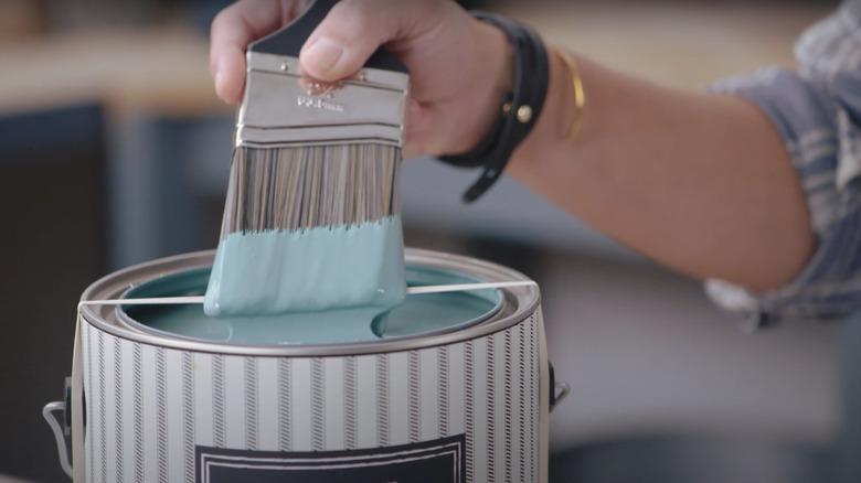 Joanna Gaines wiping excess paint off of a paint brush on a rubber band stretches around an open paint can