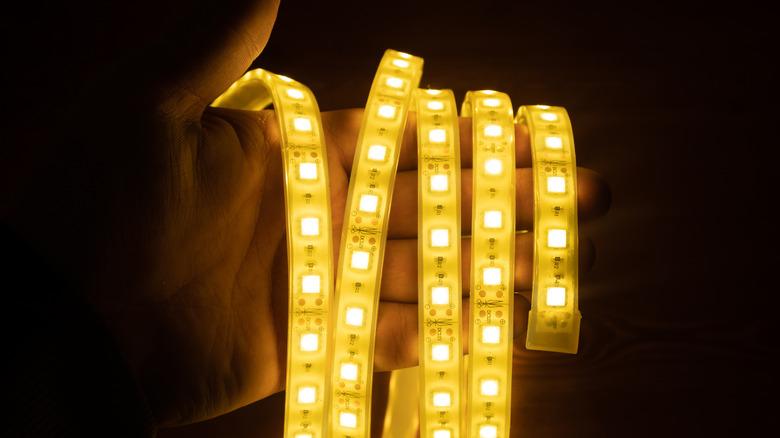 LED rope lights are wrapped around a hand. The Image is dark but illuminated by the glow of the yellow lights.