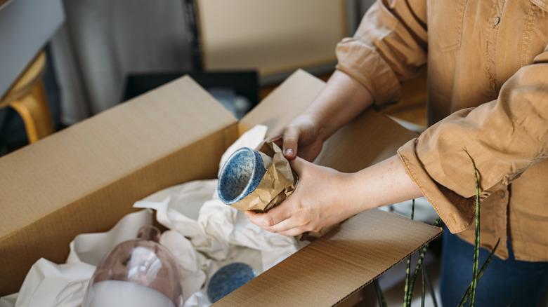 woman wrapping mugs with paper and packing them