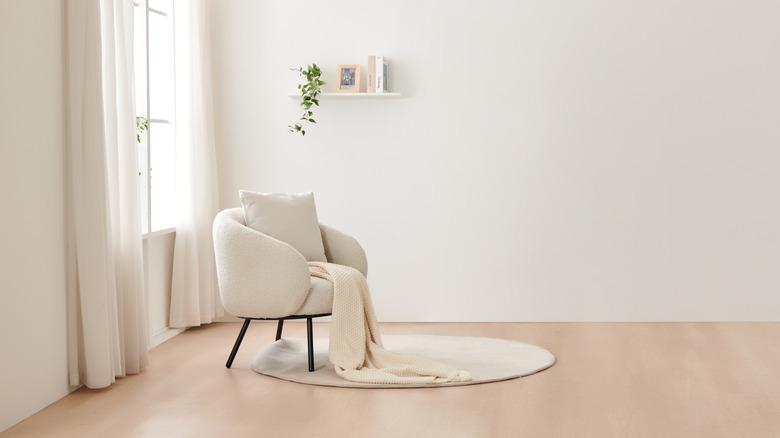 room with cream walls, cream sheer drapes around a window, cream boucle chair with cram throw, and a cream rug on a beige floor