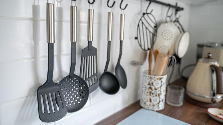 plastic and metal cooking utensils hanging on a wall