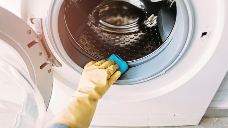 Close-up of a yellow-gloved hand washing the rubber gasket on a front-load washing machine.