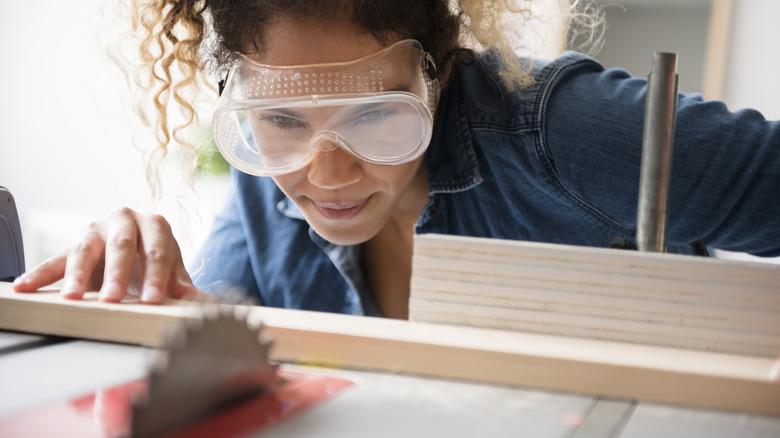 woman wearing goggles looking at blade on wood for DIY project