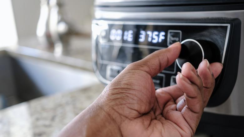 Hand turning up temp on air fryer