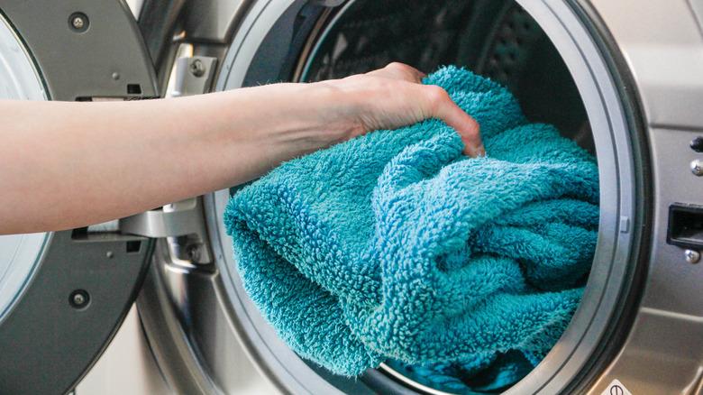 person putting bath towel in washing machine