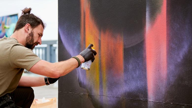 A man spray paints a black canvas with aurora-like patterns.