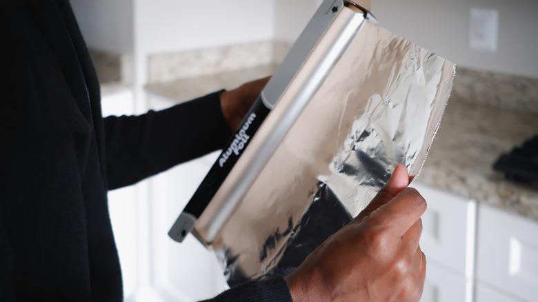 person unrolling aluminum foil in kitchen