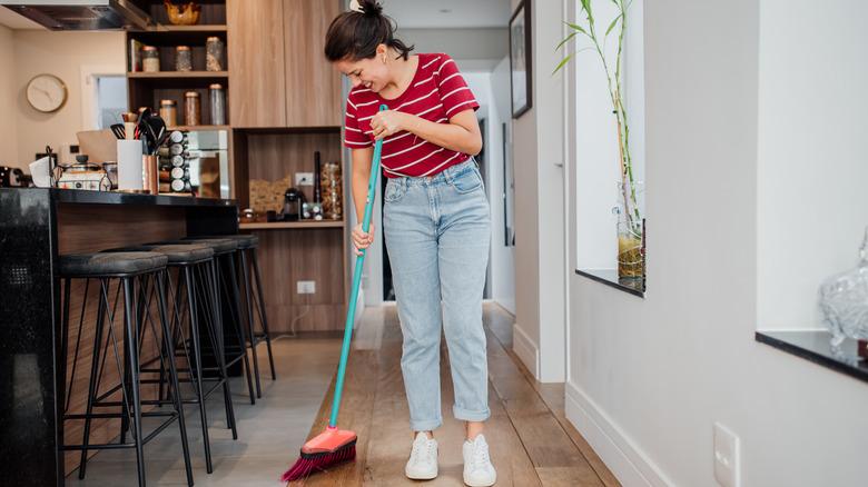 Young woman sweeping near barstools in home