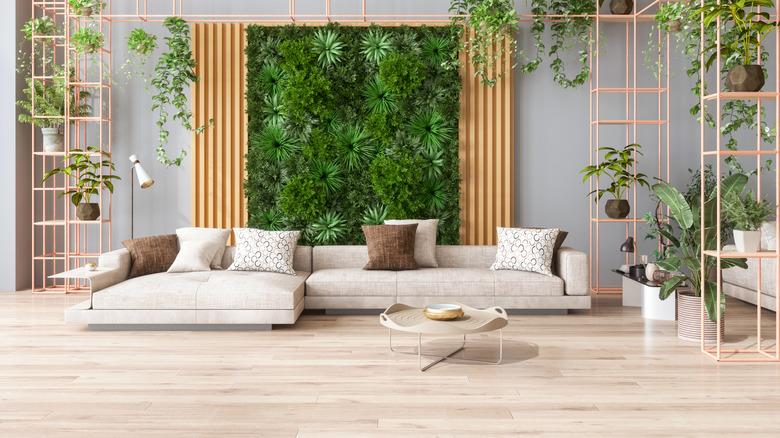 A neutral living room with raw hardwood floors, tons of indoor plants, and a wall installation made entirely of green plants