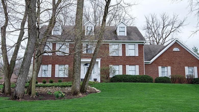 large red brick home with light gray roofing and a large lawn with trees