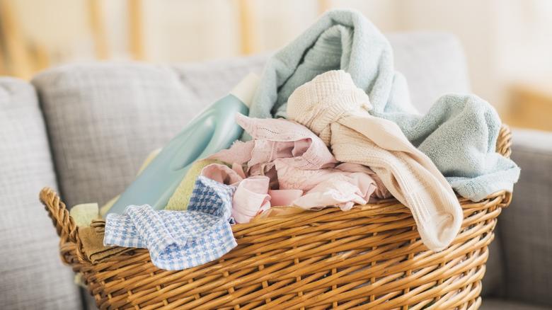 messy wicker basket of laundry full of unfolded clothes sitting on the couch