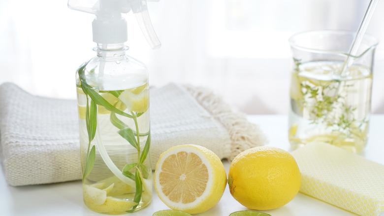 spray bottle filled with lemon water next to two lemons