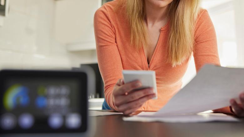 woman calculating a bill with calculator and paper while in the kitchen