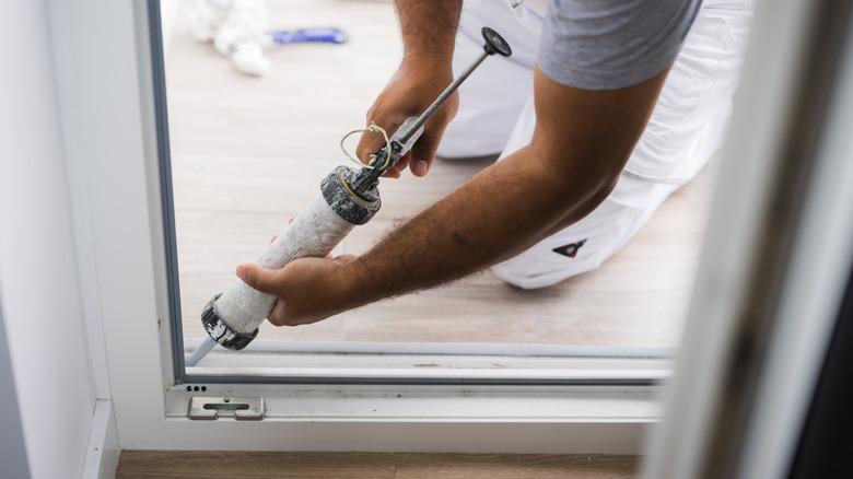 man using a silicone sealant in a caulking gun to seal a sliding glass door