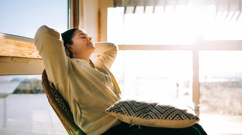 Woman reclining in papasan chair on three season glass porch on sunny day