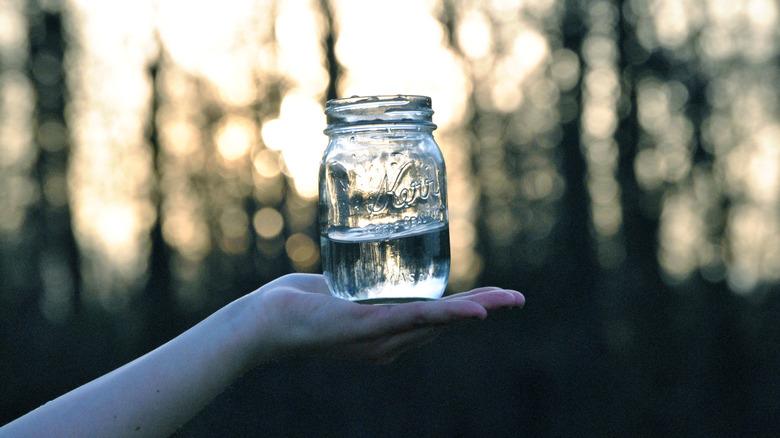 Hand holding a mason jar outside with water in it