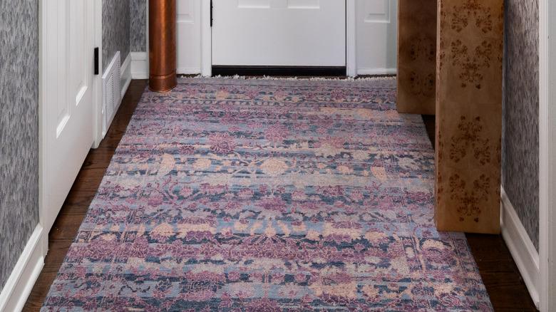 wallpapered entryway with colorful rug, hardwood floors, console, and umbrella stand