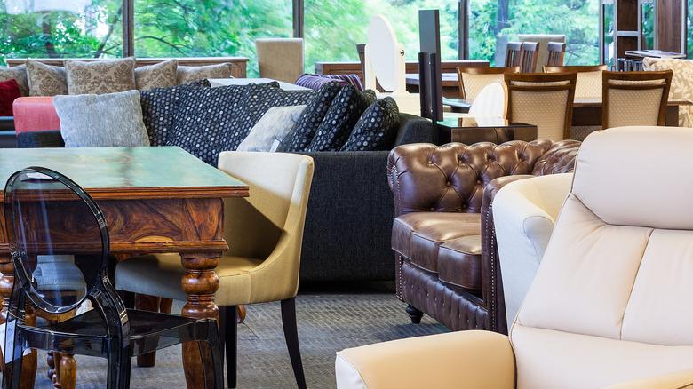 Furniture showroom featuring lots of different pieces including a black Lucite armchair, tufted leather chair, and black sofa.