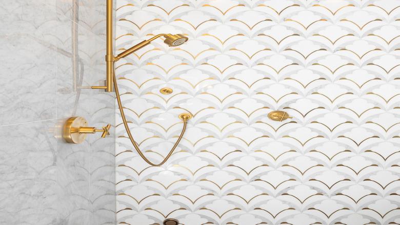 a patterned tile shower wall with gold accents and gold hardware