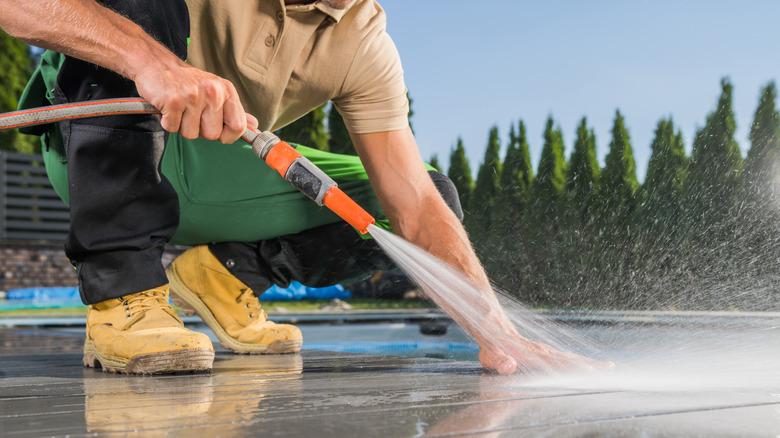 A man hosing down a composite deck and feeling the surface.