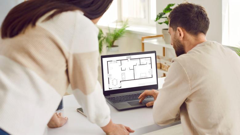 a man and woman looking at a laptop screen showing a house floor plan