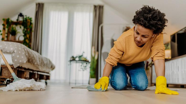 woman wearing yellow cleaning gloves and using a rag to clean a spot on her luxury vinyl plank floor