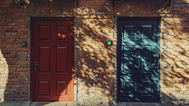 red and emerald/blue jewel toned doors on brick building with shadow of plants
