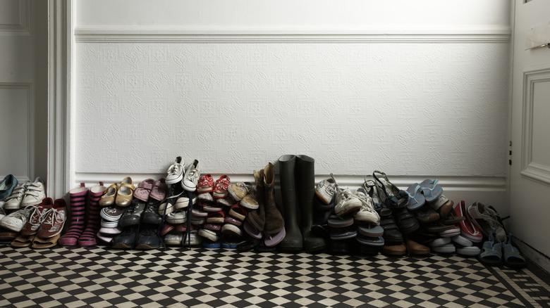 entryway with checkerboard floors and white walls that contains shoes and boots all stacked up in piles on top of each other