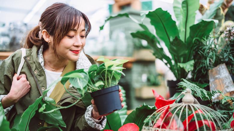 woman smiling as she picks up a plant to purchase in a store.