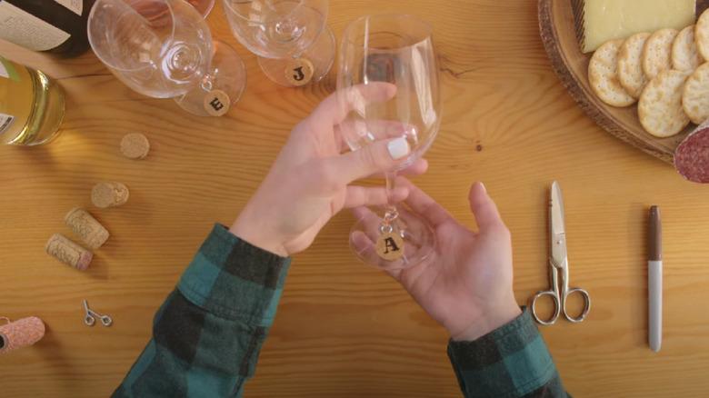 Hands holding a wine glass with a cork wine charm hanging on the base.
