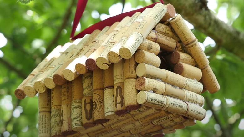 A birdhouse made of wine corks hanging up in a tree.