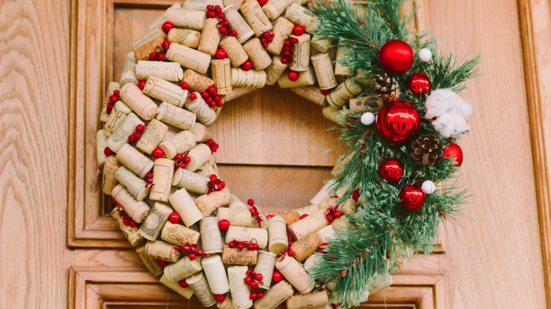 An outdoor wreath made of wine corks and pine boughs hanging on a door.